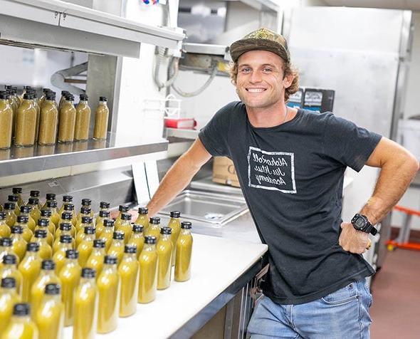 Cole Millington posing next to hot sauce bottles in a commercial kitchen